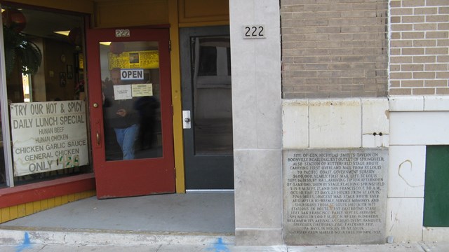 The front of a stone store front with a red door.