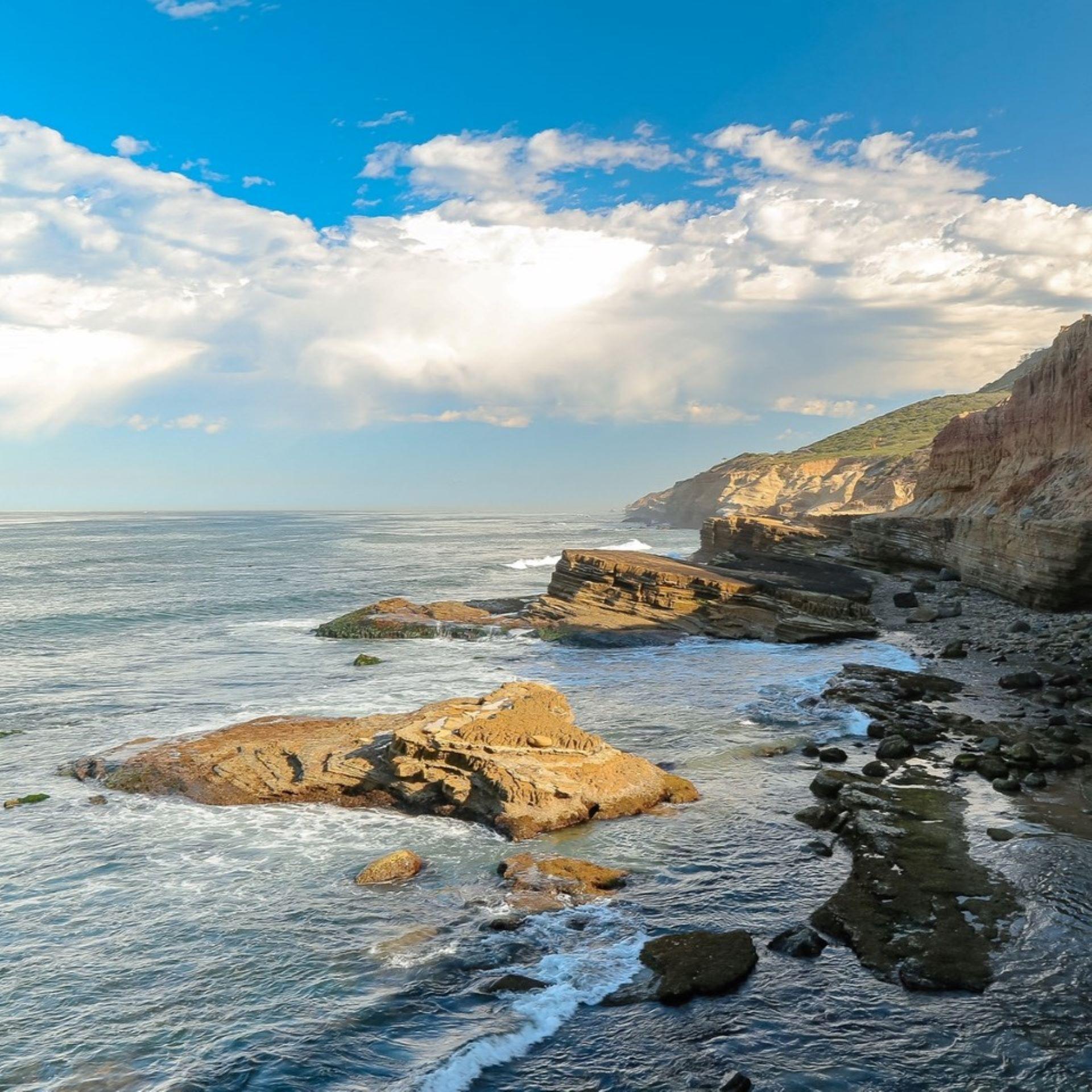 Lanscape view of Cabrillo National Monument's low-tide tidepools, with blue sky, waves, and cliffs. 