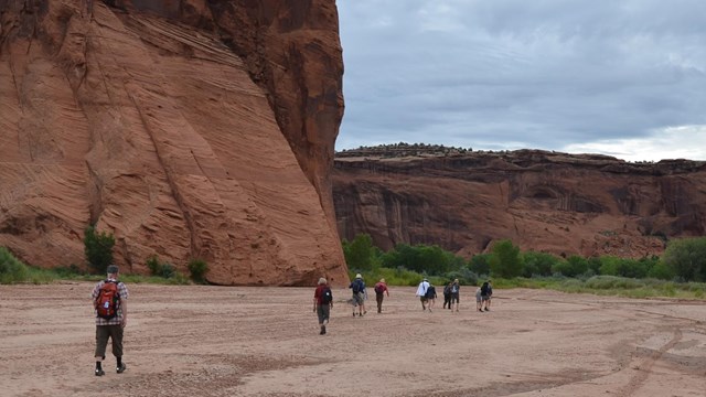 Visitors and Park Ranger walking through sand at the bottom of the canyon.