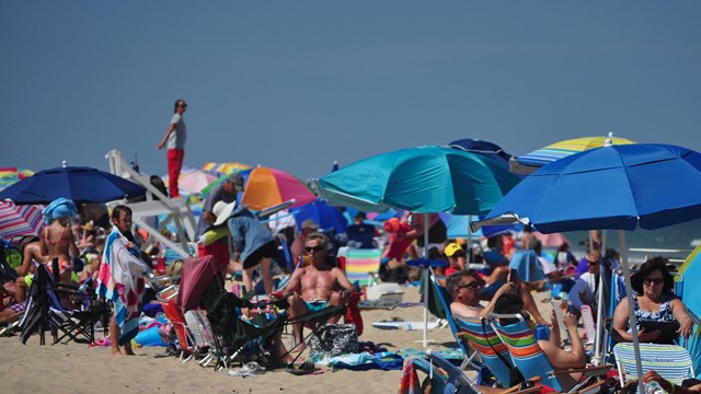 A crowded beach with people lounging under colorful umbrellas.