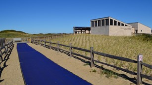 A blue mat designed for improved beach access stretches out from a grey bath house structure.