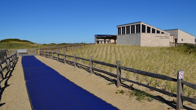A blue mat designed for improved beach access stretches out from a grey bath house structure.