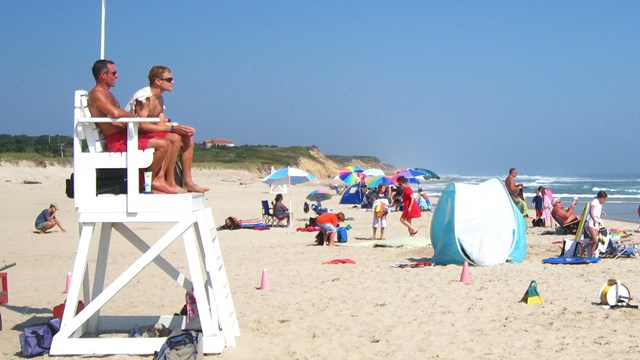 Lifeguards watch over a beach while people enjoy the sun and sand with colorful umbrellas.