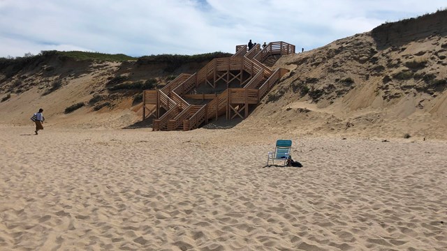 Wooden stairs lead down to a beach with a lone beach chair