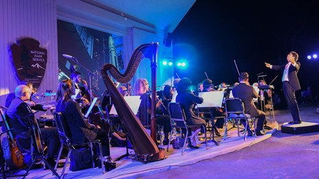 Image of conductor and orchestra with purple lighting.