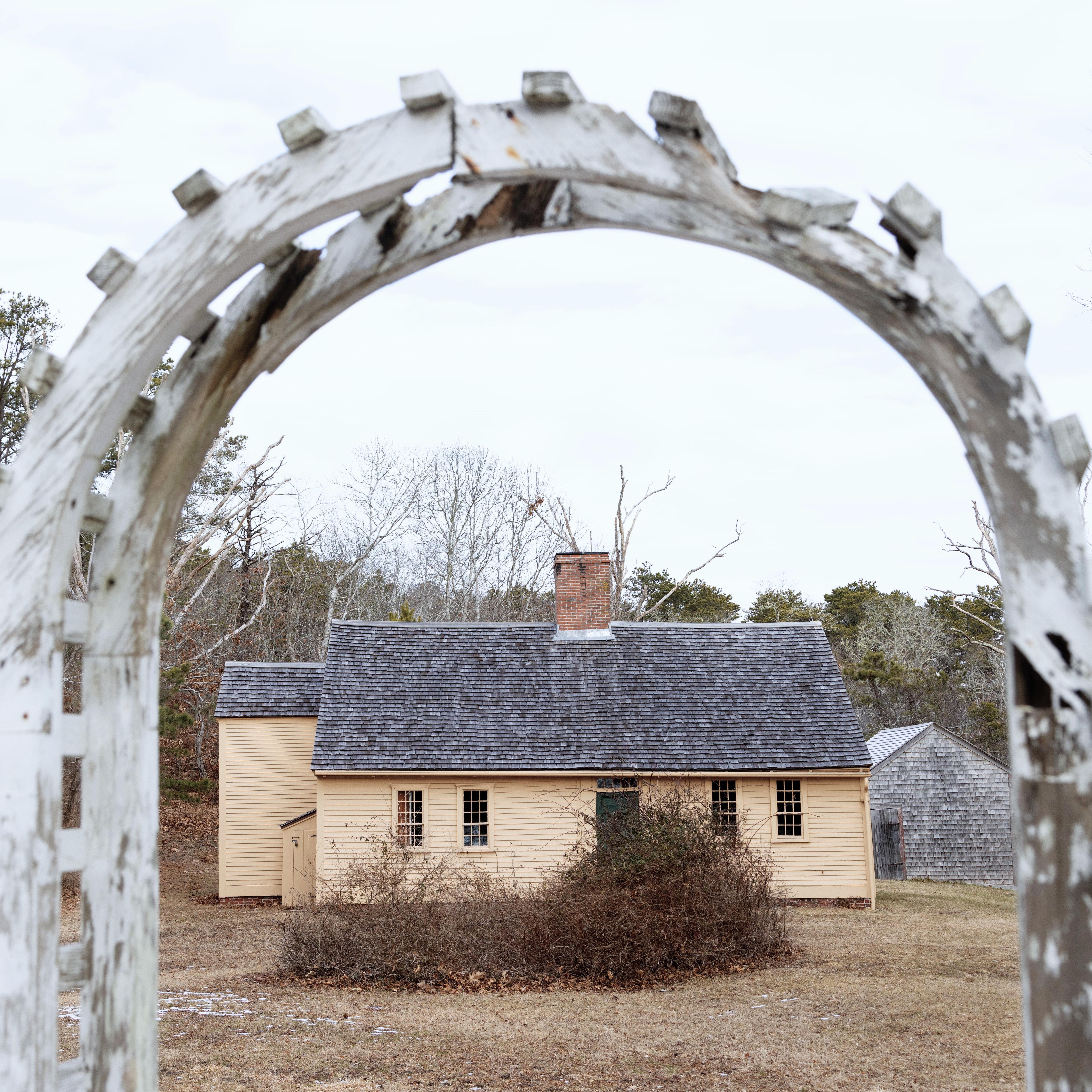 A yellow one floor house is seen through a wooden archway.