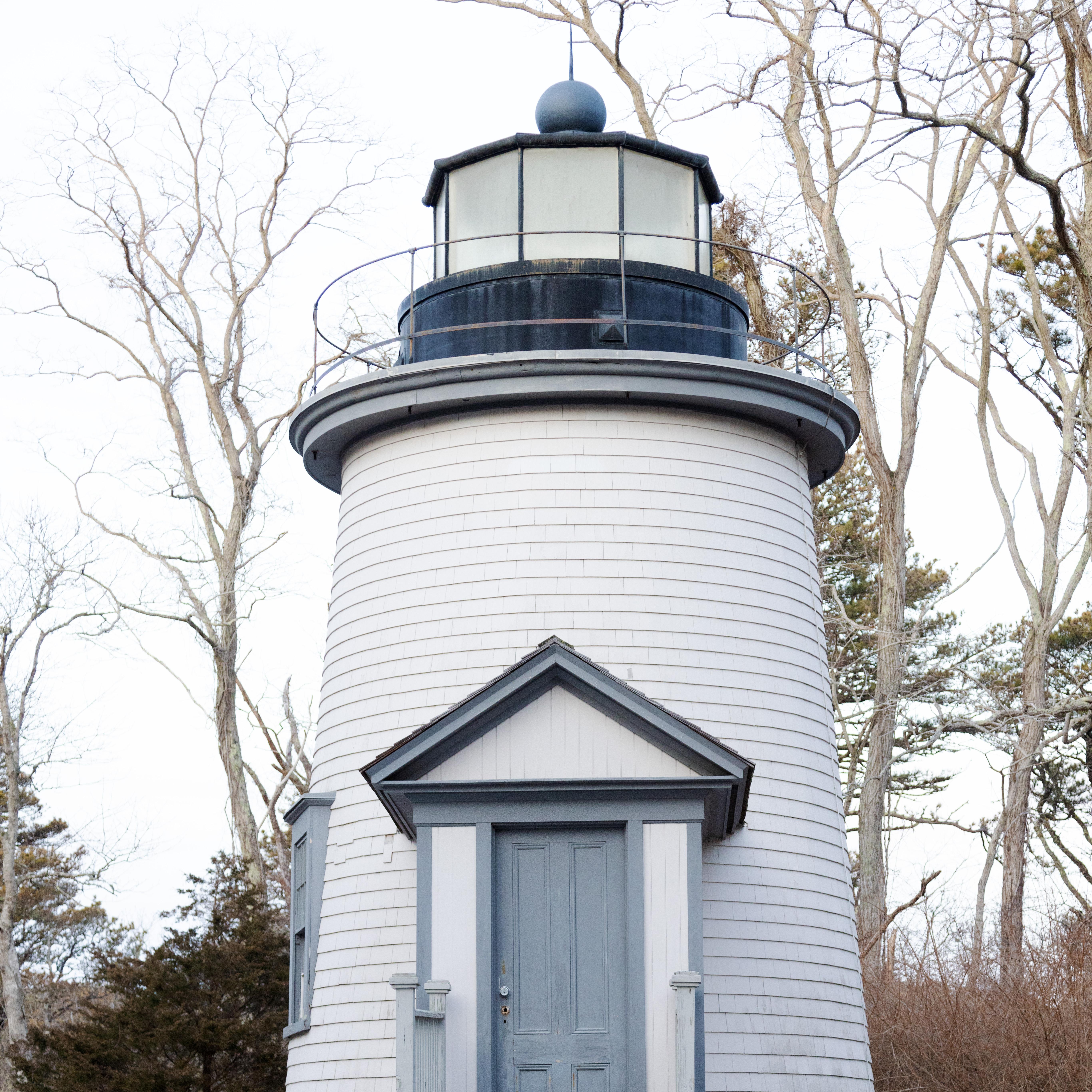 A photograph of a simple white lighthouse with wooden siding and a dormered door from the 1800s.