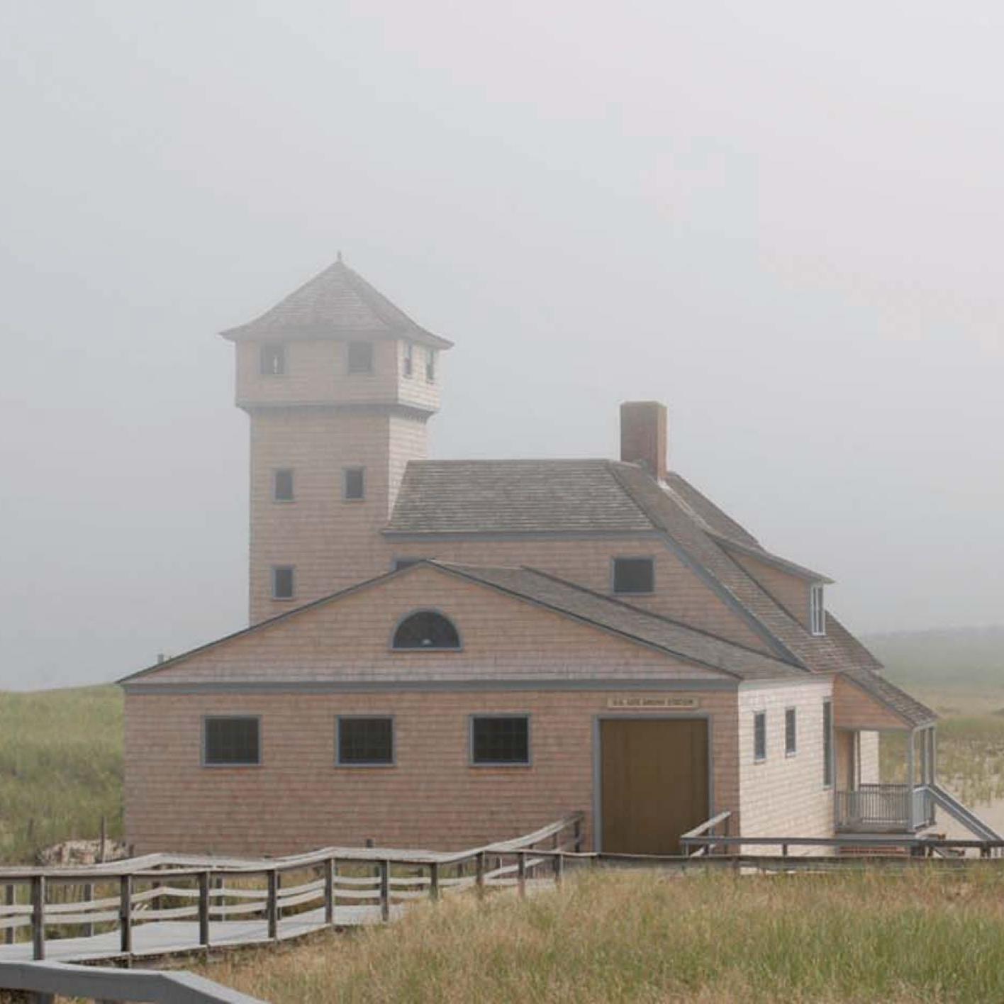 An older building on a dune surrounded by mist.