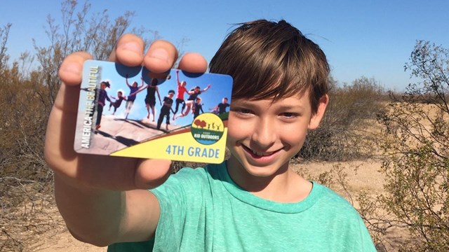 A fourth-grade student holds a Every Kid Outdoors pass for national parks