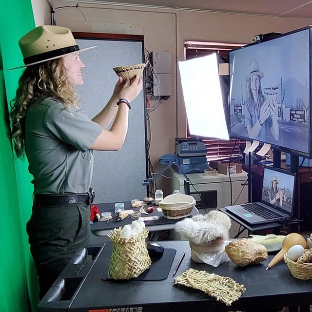 A Park Ranger holds up a props while presenting a virtual field trip against a green screen. 