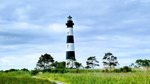 A black and White lighthouse viewed from the end of a wooden boardwalk