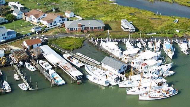 Aerial view of a marshy island with houses and small boats alongside. 