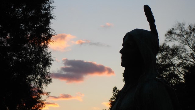 A statue of Pocahontas against a sky in sunset. 