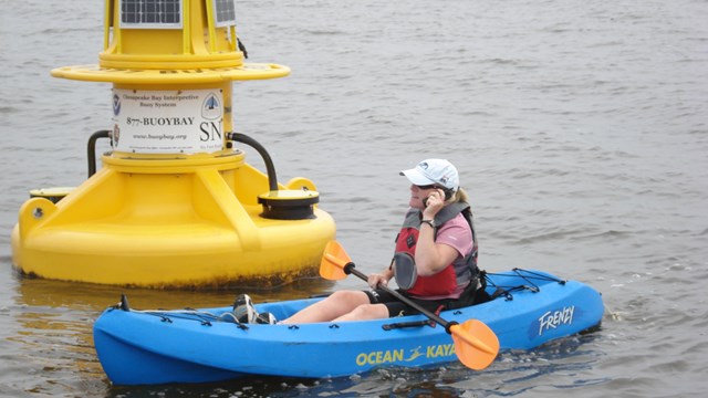 A kayaker in front of a NOAA interpretive buoy on the trail