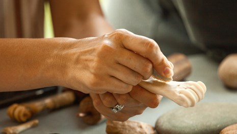 Hands use a stone tool to carve a deer bone. 