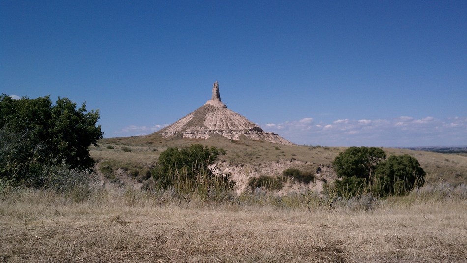 A pointed bluff landmark sticks out above a flat valley with large green shrubs.
