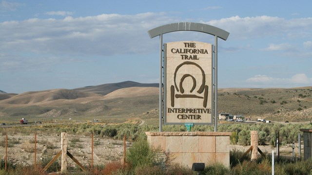 A large sign with a covered wagon symbol, in front of a distant building.