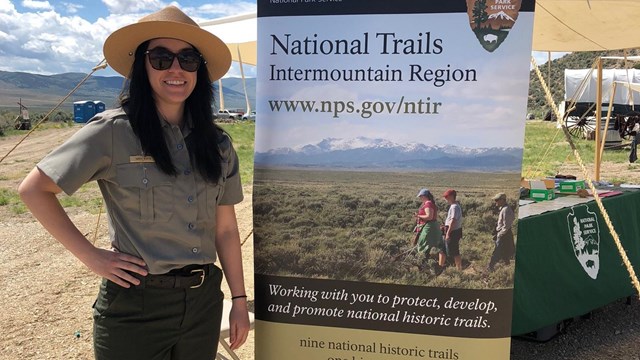 A uniformed park ranger stands next to a tall banner sign.