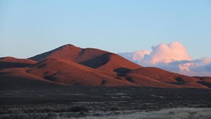 A large, smooth looking hill with distant billowing clouds.