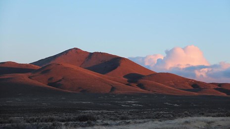 A large, smooth looking hill with distant billowing clouds.