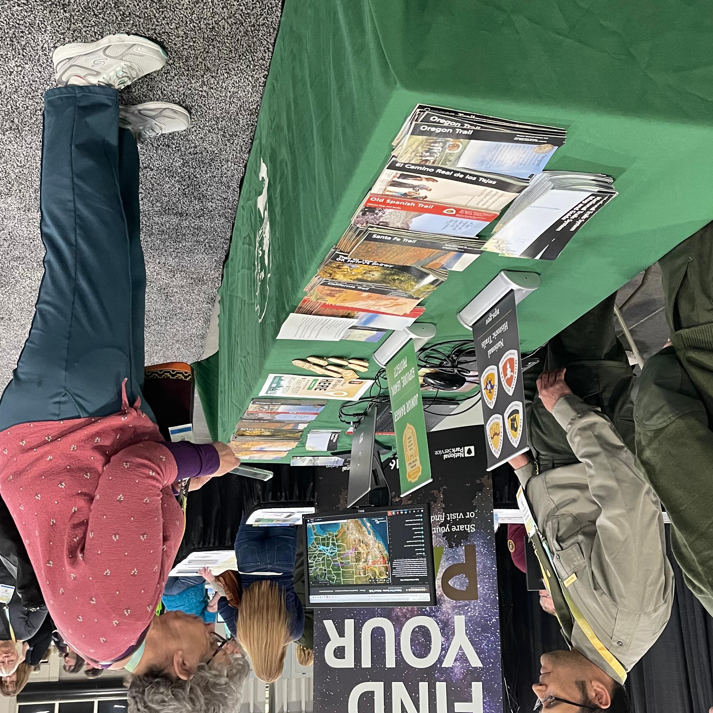 People in uniform stand at a table with brochures and literature, speaking to a person.