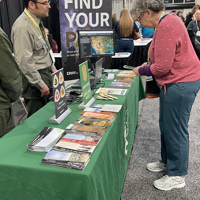 People in uniform stand at a table with brochures and literature, speaking to a person.