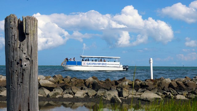 Ferry boat passing by a stone barrier with grass in the foreground