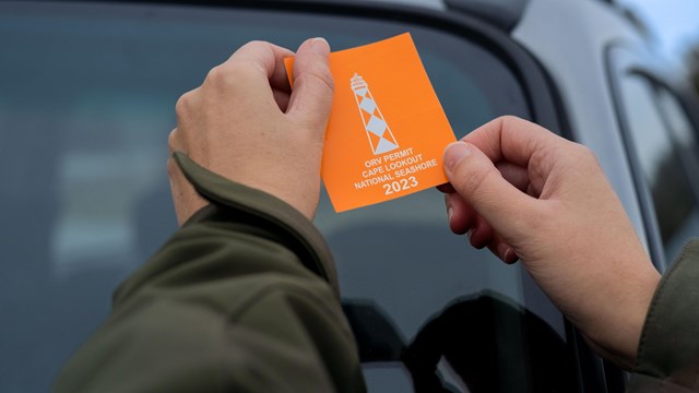 Two hands hold the 2023 ORV window decal, with blurred car in the background