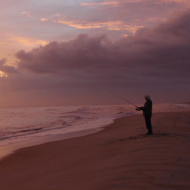 An angler on the beach at sunset.