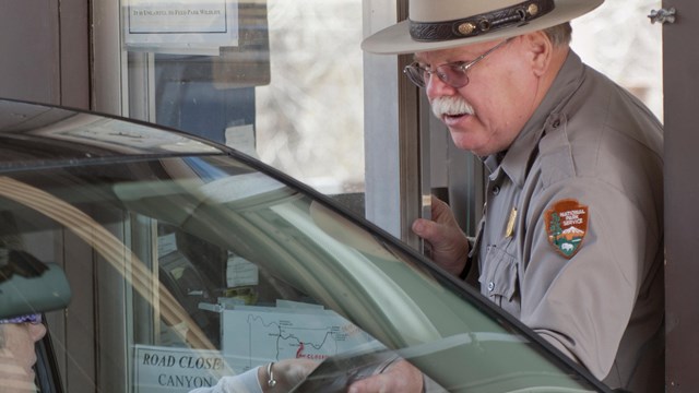 A Park Ranger greets a visitor in a car at the entrance station