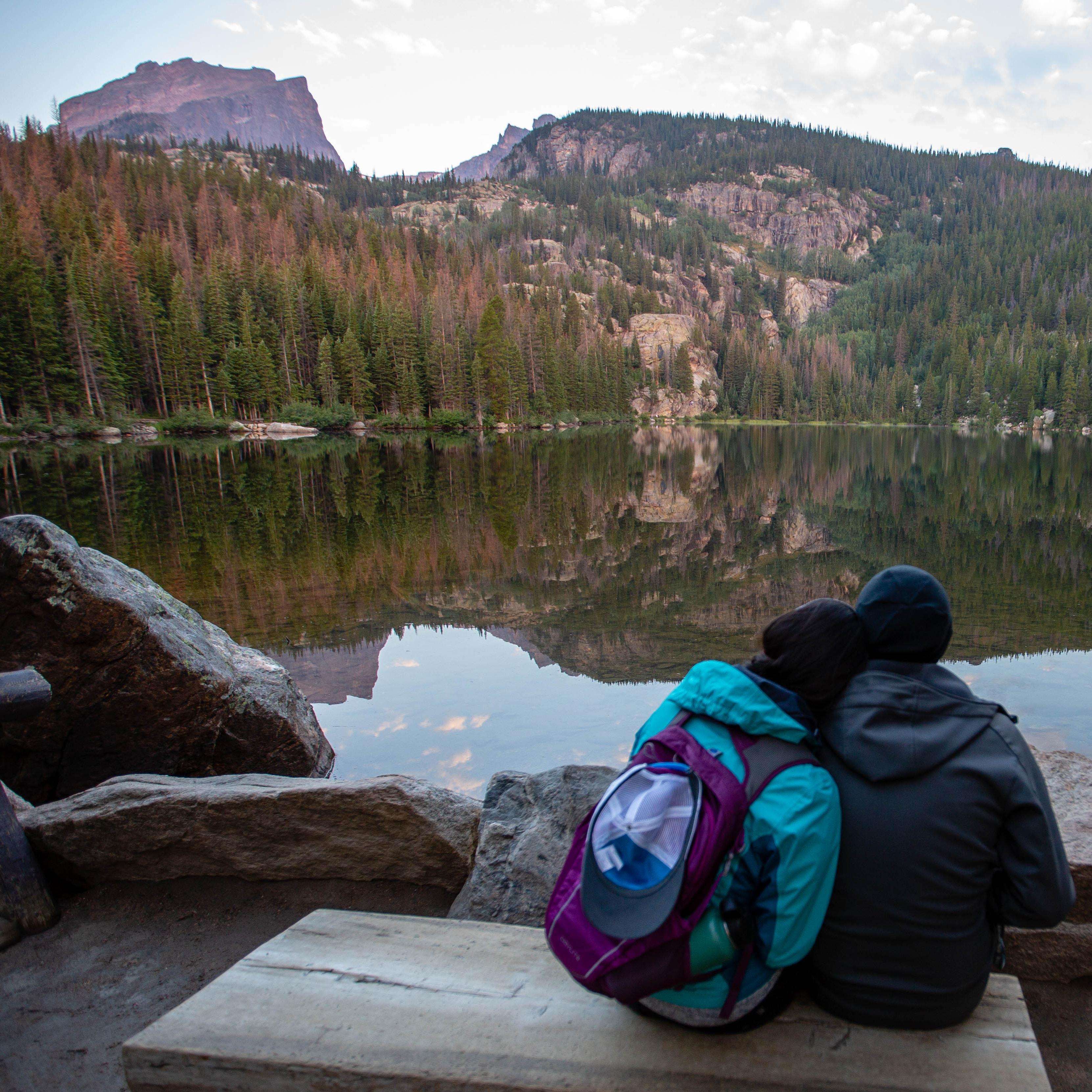 a man and woman sit on a bench looking out onto a lake and mountain during sunrise