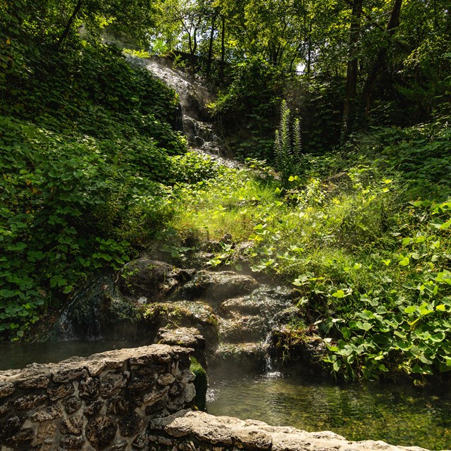 Thermal water travels into two stone pools with lush vegetation in the background.