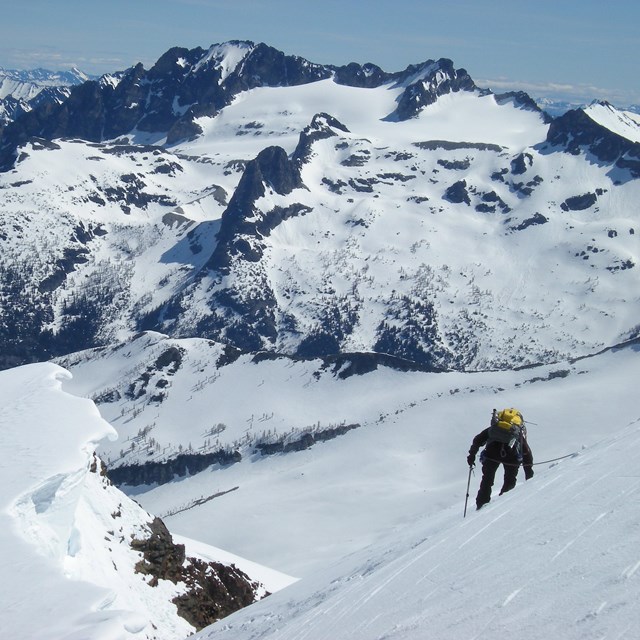 Climber on a snow-covered slope, with mountains in the background. NPS/Cori Oakes