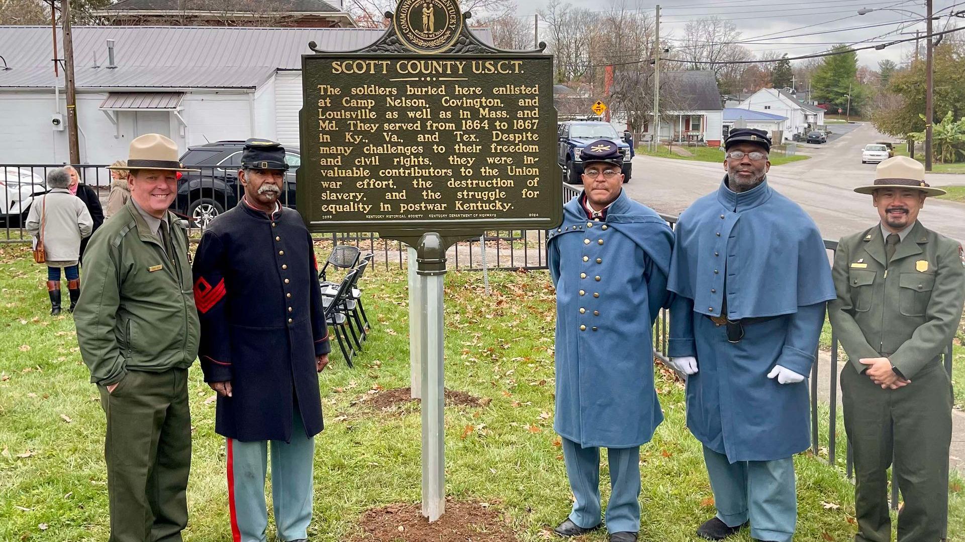NPS staff and African American living historians standing next to a green historic marker.