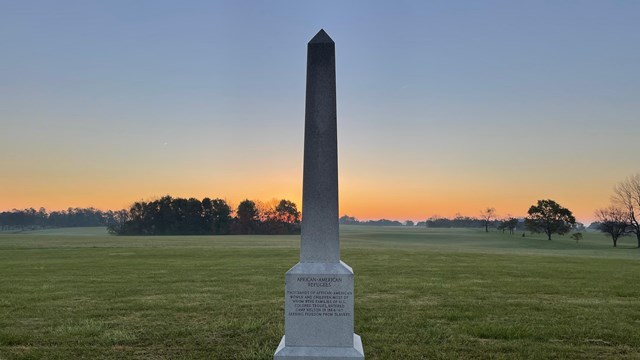 A stone obelisk on grass with trees in the background.
