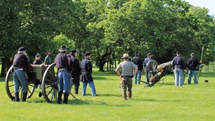 Image of reenactors portraying US Army soldiers shooting a cannon. 