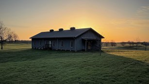 Sunset over a wooden building surrounded by green grass