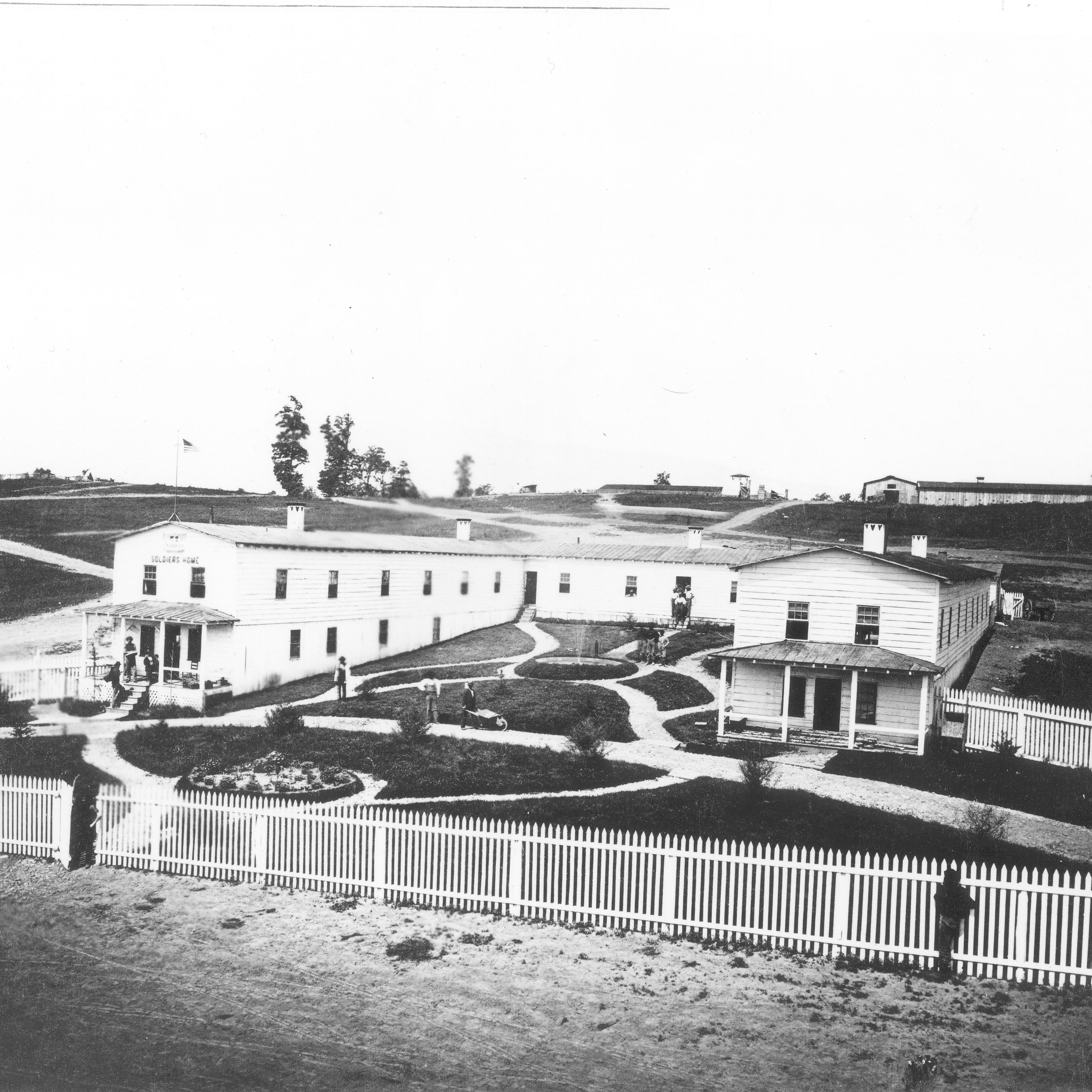 A large -shaped wooden structure with a fence, walking paths, and fountain. 