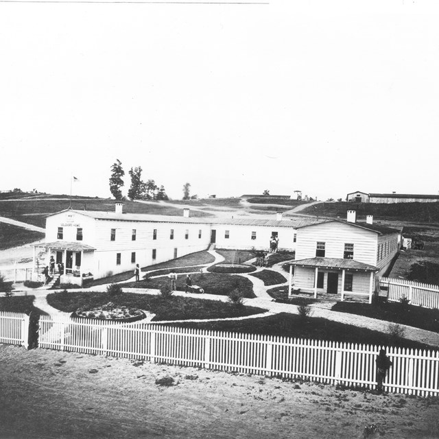 A large -shaped wooden structure with a fence, walking paths, and fountain. 