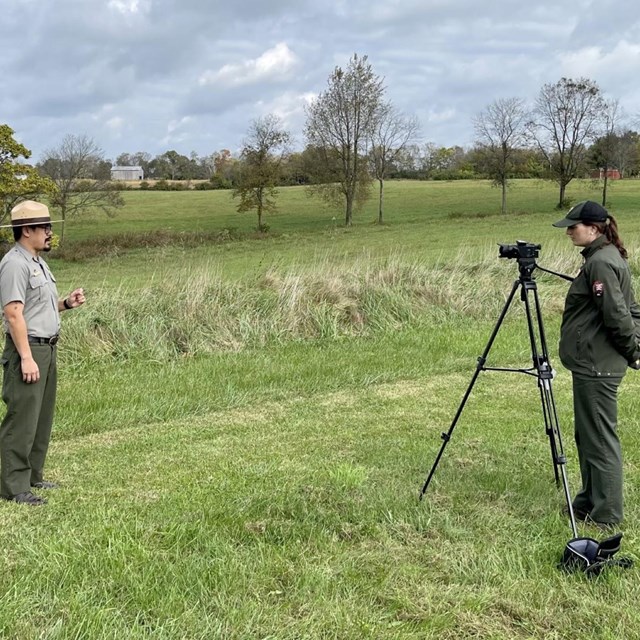 Ranger presenting in grassy fields while another ranger records with camera.