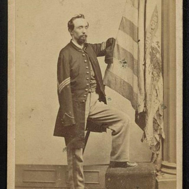 Sergeant Thomas Plunkett in US Army uniform with a torn American flag during the Civil War.