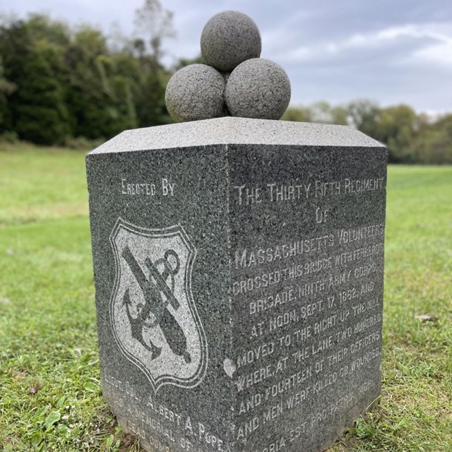 Stone memorial with three cannonballs on top and inscribed on side with symbol of the Ninth Corps.