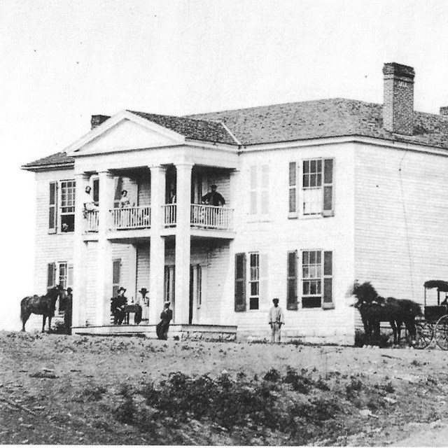 Two-story house with soldiers and civilians outside it and on second floor balcony during Civil War.