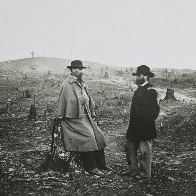 One US Army officer standing and one sitting amid a cleared field during the Civil War.