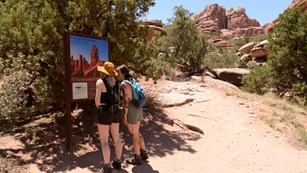 Two hikers stand at a trailhead sign