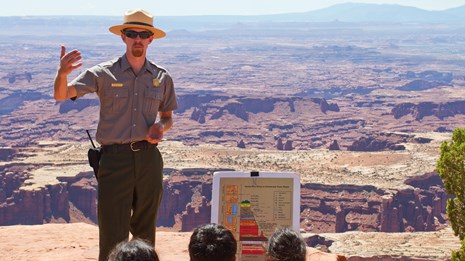 a ranger stands in front of a view of distant canyons