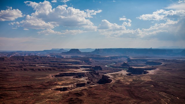 a distant view of canyons with a white puffy clouds overhead