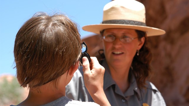 a child uses a magnifier to look at a ranger