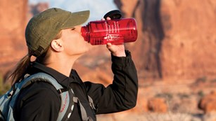 a woman drinks from a red water bottle