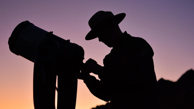 A ranger looks through a telescope at dusk